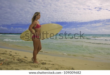 blond girl in pink bikini with surf board watching the waves