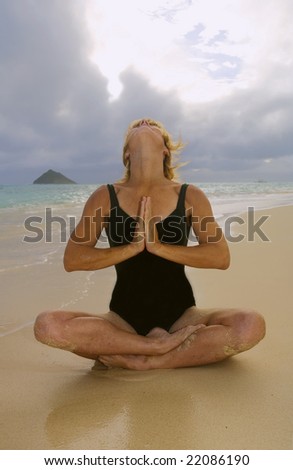A fifty year old woman doing yoga and meditation on the beach by the ocean in Hawaii at daybreak.