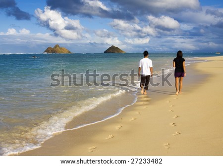 A young couple walk by the water\'s edge on a beach in hawaii in the late afternoon