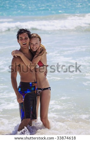 A young couple plays at water\'s edge,hugging each other, by the surf at kailua Beach, Hawaii