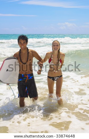 A young couple comes out of the ocean with a boogie board at Kailua Beach, Hawaii