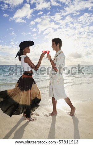 beautiful mixed race couple toast with a glass of wine at sunset on a tropical beach