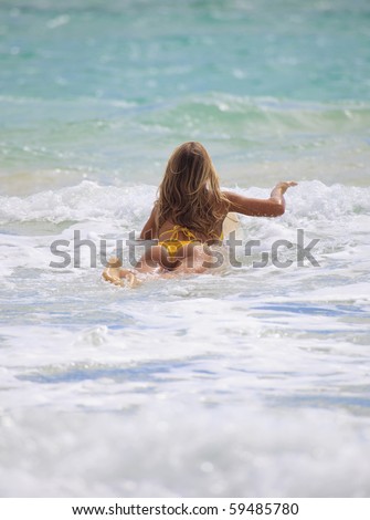 blond girl in bikini paddles her surf board towards the waves