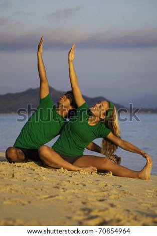 young couple doing yoga, stretches, and meditation on the beach at sunrise