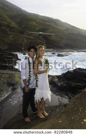 young mixed newlywed couple on lava cliffs by the pacific ocean in Hawaii