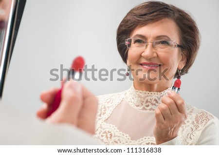 Beauty senior woman apply lipstick and smiling in mirror