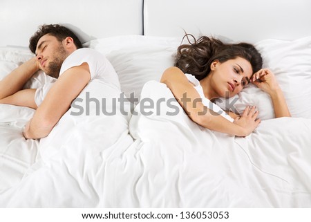 Upset young couple having disagreement lying side by side in bed facing in opposite directions