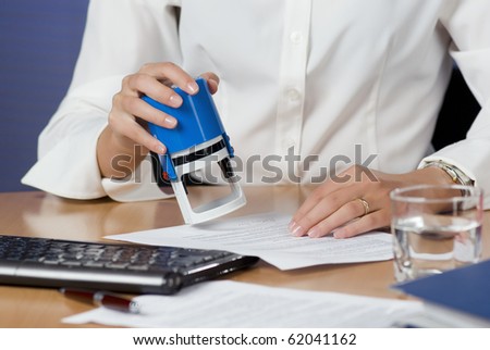 Young businesswoman (or notary public) sitting at the desk in office and stamping document