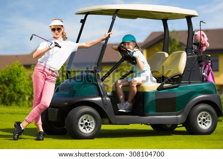 Girls posing near golf car in golf course at summer day