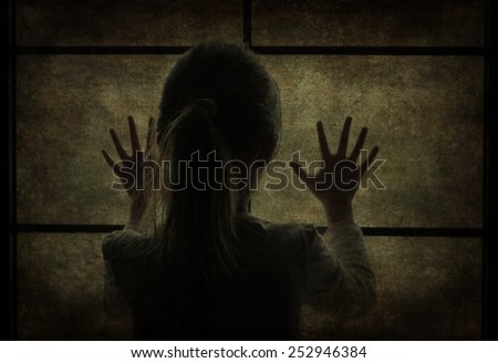 Young girl at window (in dark silhouette) hands pressed against window, pensive or wanting out?