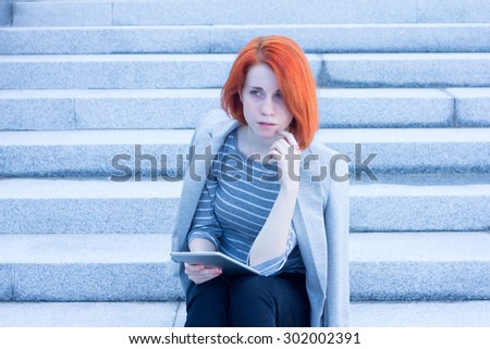 Redhead attractive woman sitting outside on the stairs with tablet