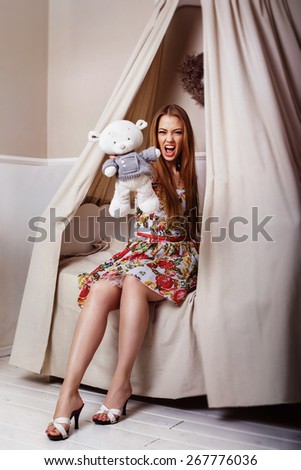 A glamour young girl is sitting on a bed, looking at camera holding a teddy bear and shouting.