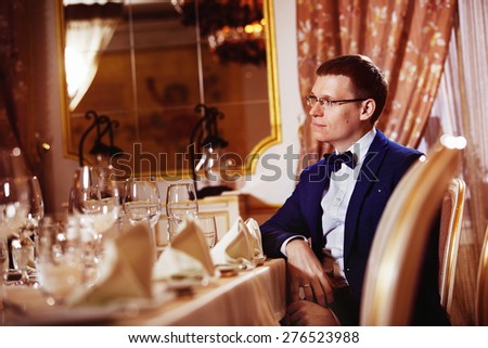 Elegant dressed businessman in glasses is sitting in luxury restaurant waiting for dinner.