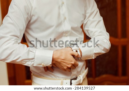 Close-up image of a man in white shirt who fastens a clock. Concept of a young man morning.