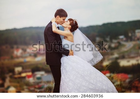 Beautiful young wedding couple is kissing on the top of the hill at natural summer background.
