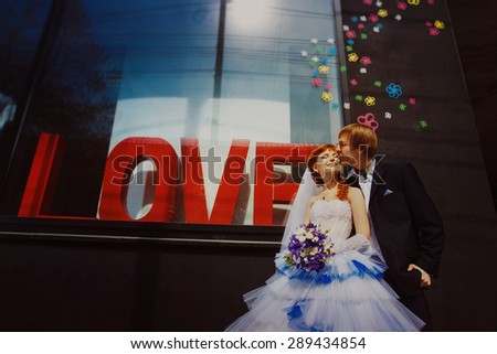 Happy wedding couple is kissing at street shop window with caption Love background.
