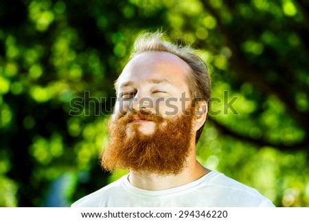 Closeup portrait of happy mature man with red beard and mustache is smiling at summer green park background.