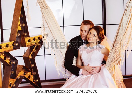 Happy beautiful wedding couple is smiling swinging in hammock at window with yellow star background.