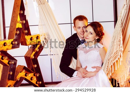Happy beautiful wedding couple is embracing swinging in hammock at window with yellow star background.