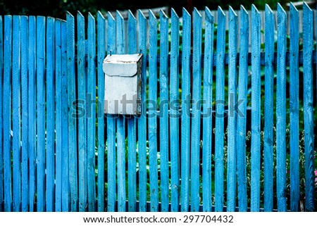 Closeup image of vintage rusty metal mail box hanging on blue wooden fence at green summer background.