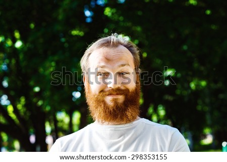 Portrait of happy funny sly mature man with red hair and beard at green summer background.