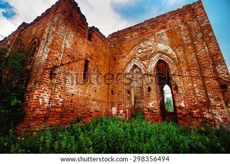 Beautiful view of old ruined red bricks church with arches at summer green grass and blue sky  background.