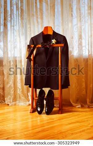 Set of elegant black shoes, suit, belt and bowtie on a wooden rack. Concept of businessman morning, wedding, retro still life.