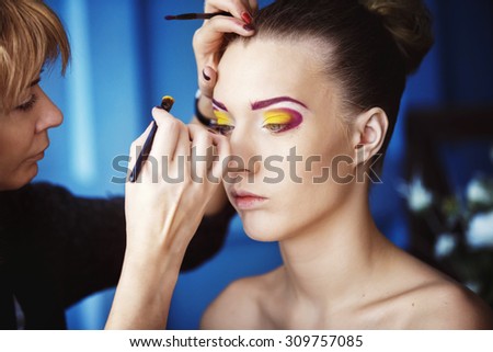 Professional makeup process. Artist is making face style of a young beautiful model at  blue studio background.