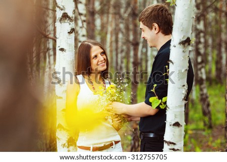 Young man is presenting girlfriend flowers in forest at birch trees background.