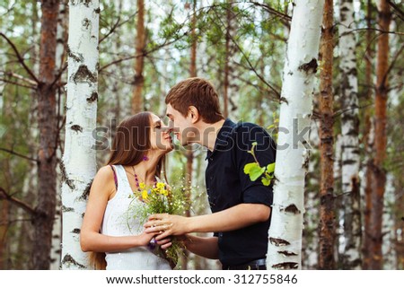Young beautiful couple is kissing in forest at birch trees background.