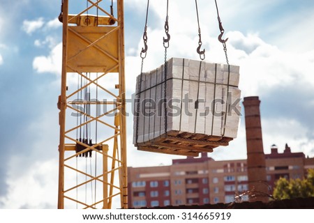 Closeup image of crane lifting heap of bricks at blue sky summer background.