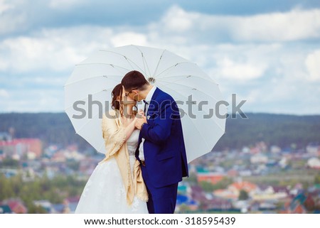 Young happy wedding couple with white umbrella is kissing at hill top at blue sky view background.