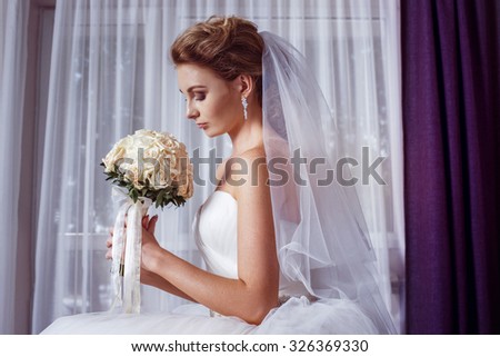 portrait of beautiful young bride holding roses wedding bouquet at white curtain background.
