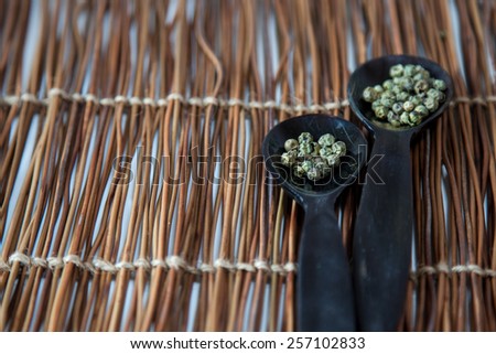 Two wooden spoons full of green peppercorns on a wooden background