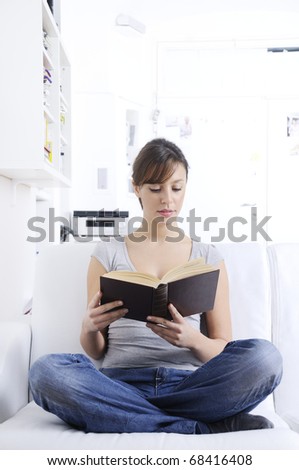 woman reading book in home interior, smiling and looking in camera; concept of relax and entertainment