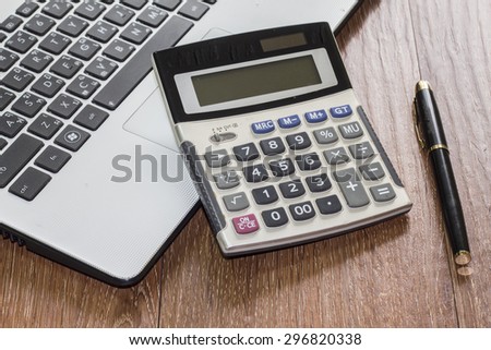 Office desk with laptop computer, calculator and  pen  on wooden background
