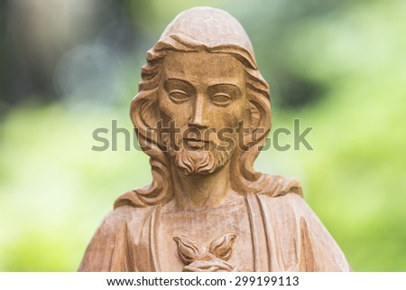 Wooden sculpture of Jesus Christ with burred nature background, close up