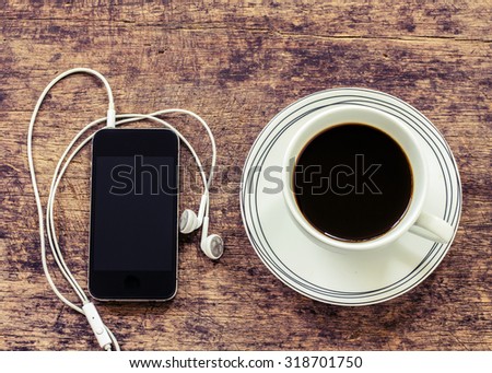 black coffee with white earphones attached to smartphone on wooden background, vintage color