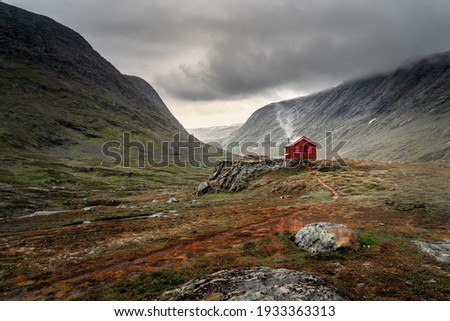A single small red cabin billows smoke from it's tiny chimney in the remote gorge of central Norway. The distant dark clouds give the feeling of isolation and remoteness. Shot during autumn 