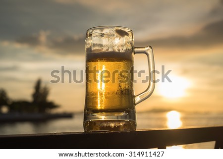 Cold Beer in the mug with the sunlight  and Sea background (Selective Focus Point)