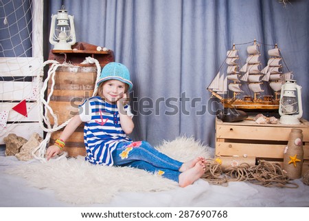 Beautiful girl in a hat sitting barefoot near the barrel, marine networking and cables. Cute little girl smiling on the background of summer sea scenery. Happy and carefree childhood