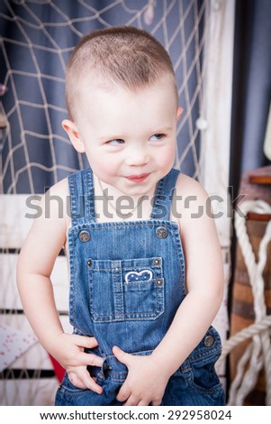 Cute kid with big gray eyes in denim overalls playing among the maritime decor.Handsome boy looking curiously into the frame.Handsome boy looking curiously into the frame. Boy hesitate.