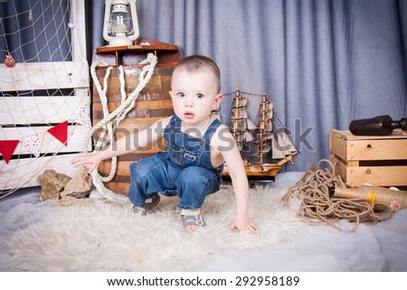 Cute kid with big gray eyes in denim overalls playing among the maritime decor.Handsome boy looking curiously into the frame. boy looking curiously into the frame.\
baby crawling on the skin.