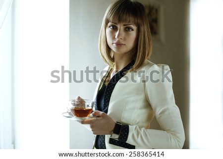 The woman at the window with a cup of tea. Woman - office worker drinking tea. Break for tea. Office style women. Cup of tea in her hands.