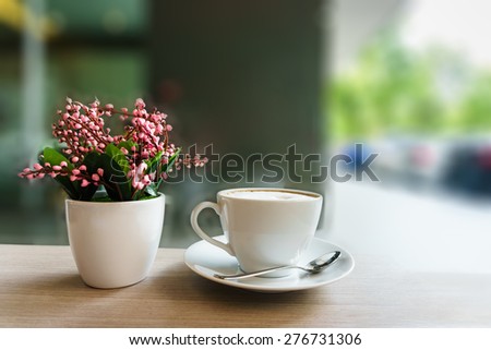coffee cup and pink flower on wooden table in coffee shop