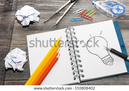 Office supplies and an open book with a drawing of a light bulb