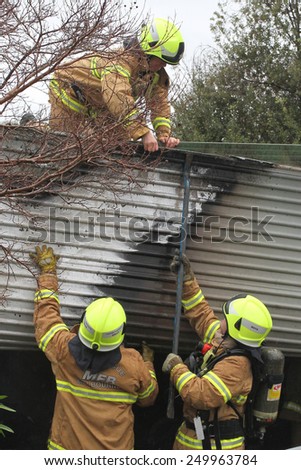 Melbourne, Victoria, Australia - 2011 July 10: Fire fighters supporting colleague on roof gaining access to a garage on fire in an residential area.
