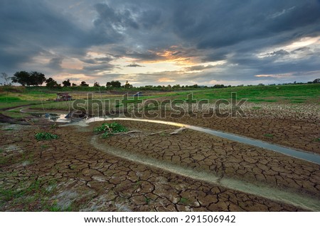 Dry river on drought parched ground and effect of sun beam in dark sky clouds before the rain.