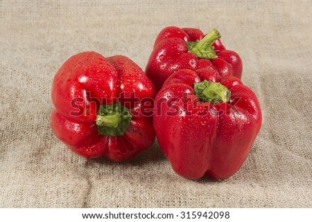 Three red sweet peppers on a burlap canvas