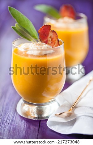 Pumpkin soup served in glasses with whipped cream, bacon and sage